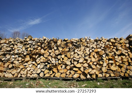 Firewood logs piled up in field on blue sky background