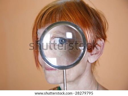 Red haired woman with blue eye peering through a magnifying glass