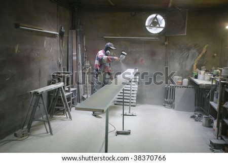 Man painting with spray paint gun in his home workshop