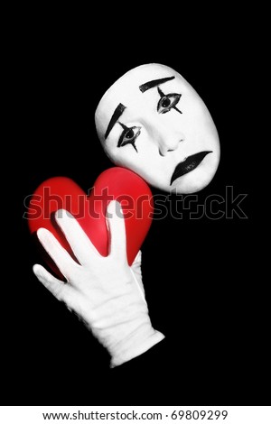 Mime with red heart. Actor mime with black and white make-up holding red heart in the hand. Isolated on black background.