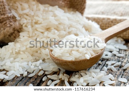 White long uncooked rice on wooden spoon