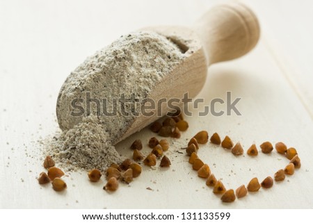 Buckwheat flour in wooden spoon. Buckwheat cereal and heart shape