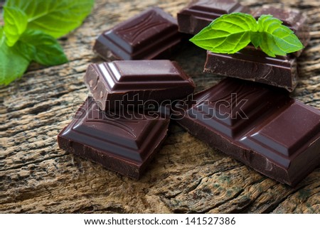 Dark chocolate pieces with a leaf of mint on wooden background