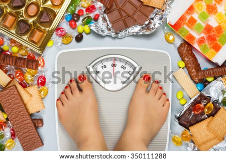 Unhealthy diet - overweight. Feet on bathroom scale and chocolate, jelly cubes, candies, chocolate bars, cookies, donuts