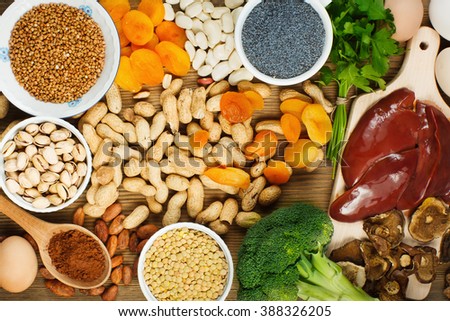 Collection iron rich foods as liver, buckwheat, eggs, parsley leaves,dried apricots, cocoa, lentil, bean, blue poppy seed, broccoli, dried mushrooms, peanuts and pistachios on wooden table.