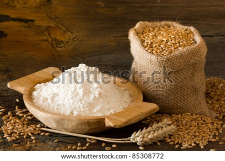 Flour in homemade wooden bowl and wheat in burlap bag