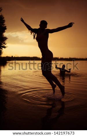 Slender young girl jump in river at sunset