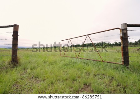 old  iron farm gate swings open on wooden posts