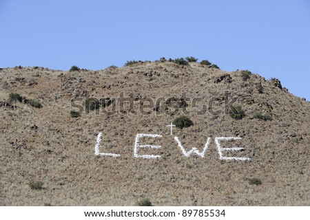 sign made stones painted white and a cross on a hillside in the karoo, northern cape, south africa. lewe is afrikaans for life.