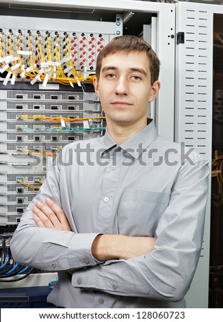 The telecom engineer stand in data center near telecommunication equipment.