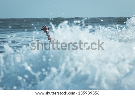 Hand of drowning man trying to swim out of the stormy ocean.