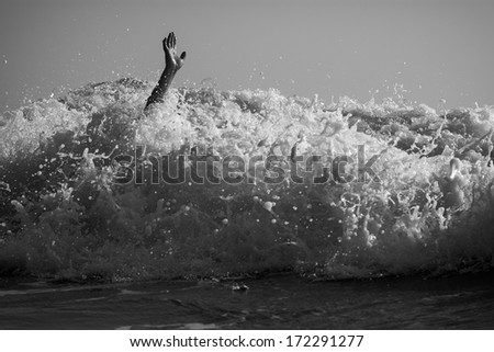 Hand of drowning man trying to swim out of the stormy ocean. Black and white photo.