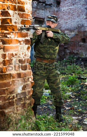 Soldier or militiaman in camouflage with assault rifle fighting in ruins
