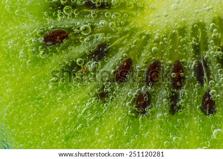 Kiwi fruit in water with bubbles over green background.
