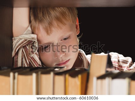 The boy at a bookcase gets the book. The boy attentively looks at the book. Copy-space.