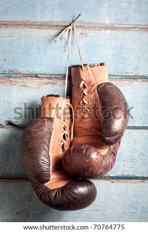Brown old boxing gloves with a lace over old blue wall with peeling paint