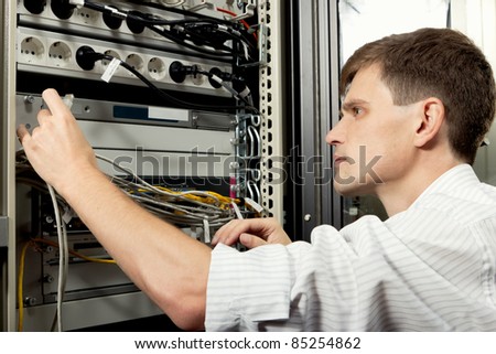 The engineer stand in datacenter near telecommunication equipment and looking at ethernet path cord.