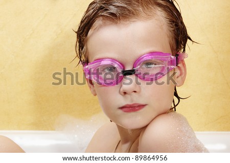 Cute boy have fun in the bathroom. The boy in the foam bath and swimming goggles.