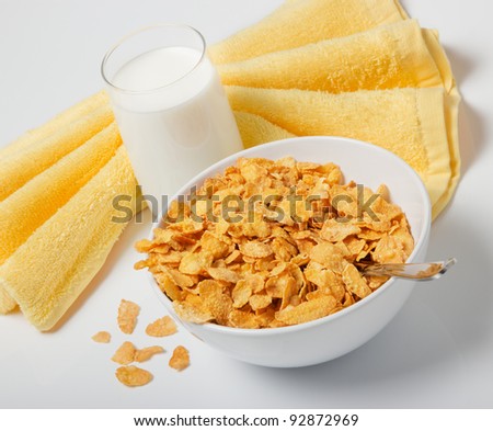 Corn flakes in deep plate with spoon, glass with milk and yellow towel. A breakfast.