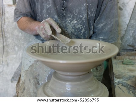 A man shapes pottery as it turns on a wheel.