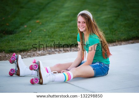 Pretty teen girl in roller skates smiling as she sits on the sidewalk