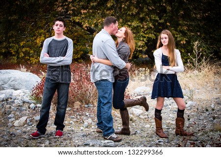 Happy couple kissing as their teen aged children look on in disgust