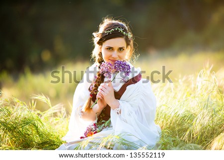 Beautiful young woman in historical clothing holds flowers up a handful of flowers