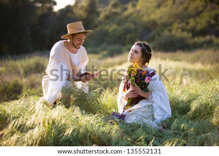 Romantic young man in historical clothing reads to a dreamy young woman with flowers