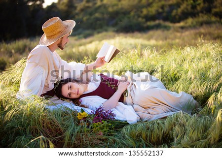Romantic couple in historical clothing relax and read in a country setting