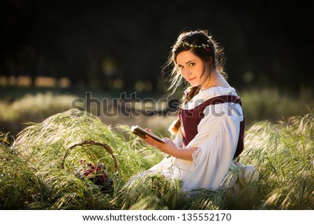 Beautiful girl reading a book in a country setting, dressed in historical clothing