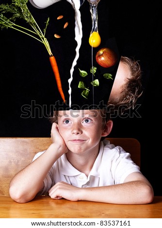 Food for thought.  Happy school child sitting at desk while his head is being filled with nutritious foods.