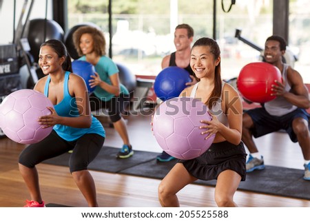 Multi-ethnic gym class doing squats with medicine balls