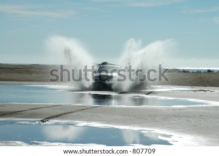 A four-wheel-drive ploughs through the water between the sand dunes.