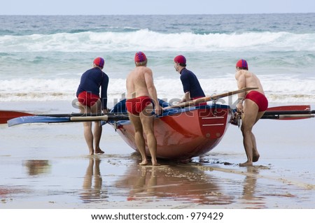 A surf boat team drag their boat across the sand to the water.