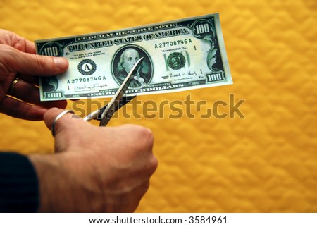 man cutting a one hundred dollar banknote with scissors