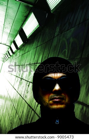 man with black glasses and a cap in front of a green subway tunnel