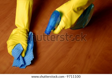 detail of a hand with working glove and spray bottle cleaning a wood surface