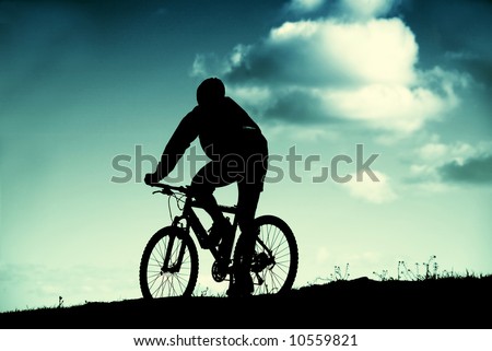 cyclist in silhouette in front of a blue sky with clouds