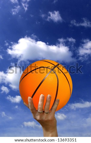 female hand holding a basketball over a blue sky