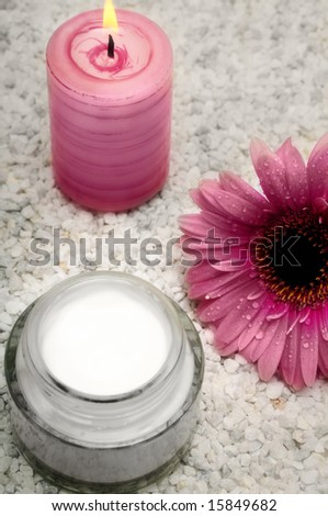 cosmetic cream in a jar, with candle and flower on white stones