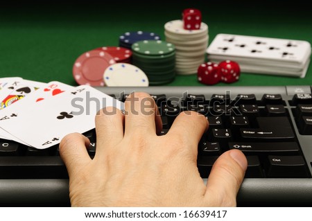 hand on computer keyboard with playing cards chips and dices in background
