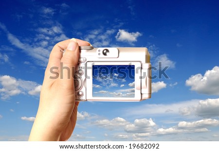 female hand holding a point and shoot camera at a blue cloudy sky