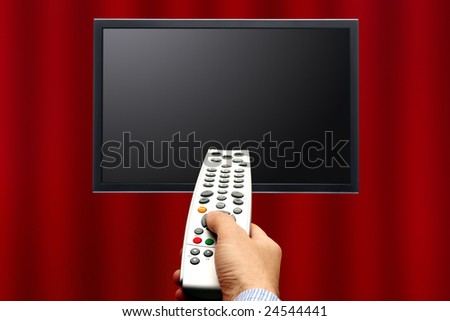 male hand pointing a remote control to a screen in front of a curtain background