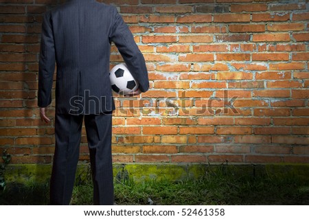 man in suit standing in front of a wall and holding a soccer ball