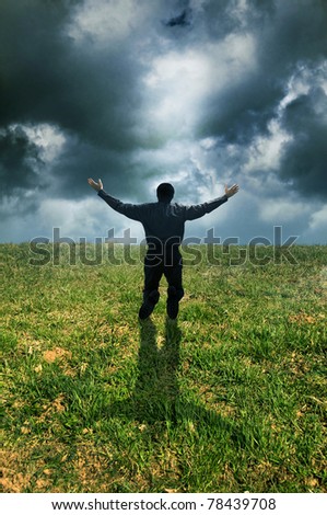 man on knees in a meadow with open arms in a prayer gesture