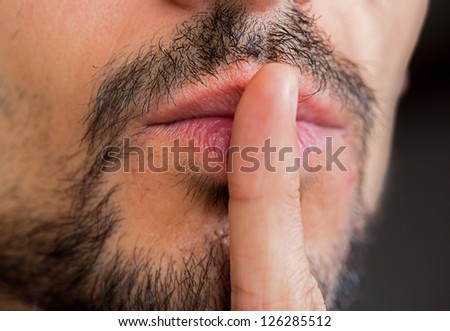 Caucasian man with stubble and finger over lips asking for silence