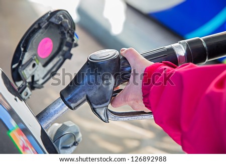 Woman left hand pumping gasoline fuel at gas pump in car at gas station.