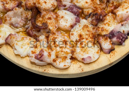 cooked octopus slices dressed with paprika over wooden plate and black background