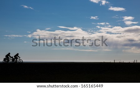 Cyclists silhouette against blue sky and clouds