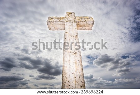 Antique stone cross covered with green lichen against cloudy sky